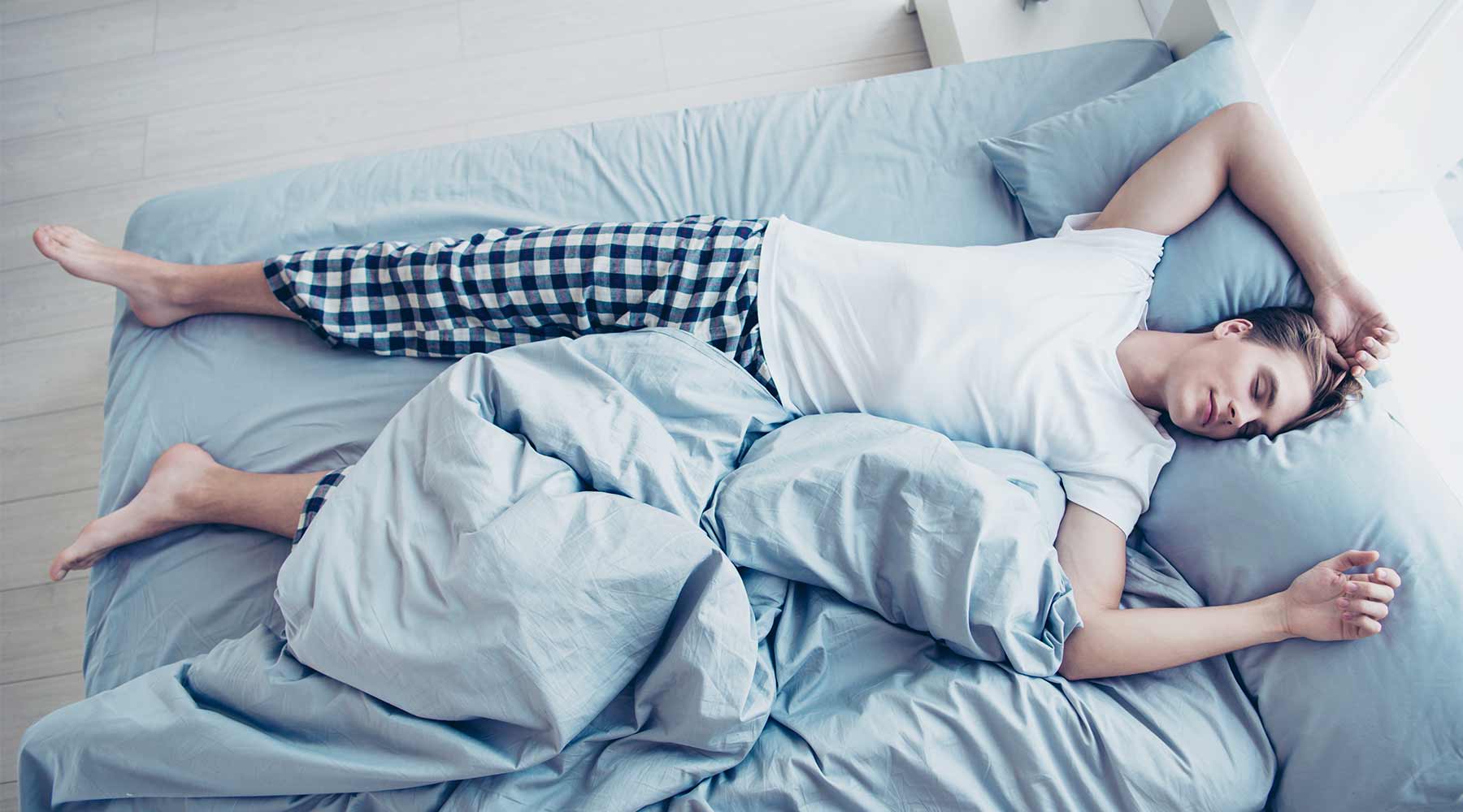 smartsleep Schlafmagazin Junger Mann liegt morgens halb zugedeckt im Bett